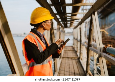 Black Woman Wearing Helmet And Vest Working With Tablet Computer In Port