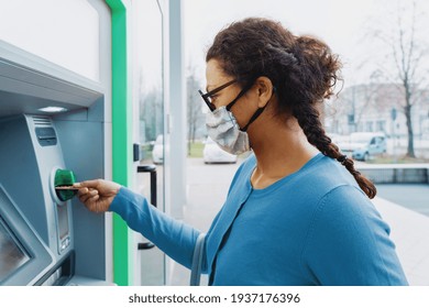 Black woman wearing protective mask while withdrawing money at ATM.
