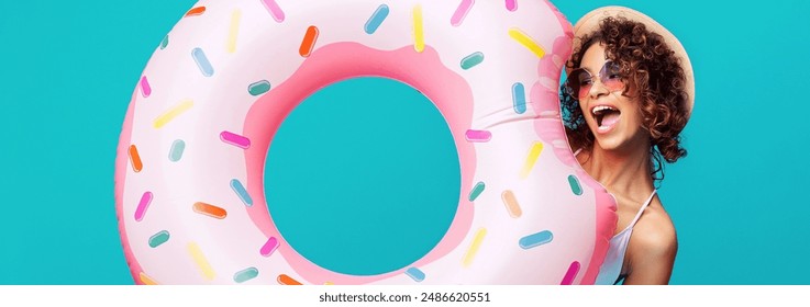 Black woman wearing a straw hat and sunglasses smiles and holds up a giant, pink inflatable float shaped like a donut. The float is covered in colorful sprinkles - Powered by Shutterstock