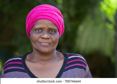 A Black Woman Wearing A Stripped Top And A Bright Pink Head Scarf.