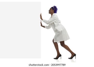 Black Woman In White Lab Coat Is Pushing Empty Banner And Laughing. Side View, Full Length Studio Shot Isolated.