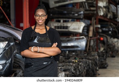 A black woman who owns a business stands with arms folded, smiling and looking at the camera on blur factory background. A black worker stands at the auto parts factory in Business onwner concept