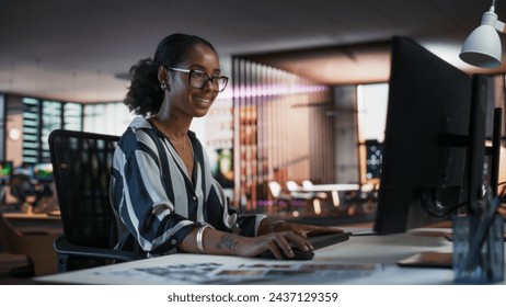 Black Woman Working on Desktop Computer in Creative Office. African American Marketing Manager Writing Email Messages, Developing Social Media Strategy, and Researching Project Plan Details Online - Powered by Shutterstock