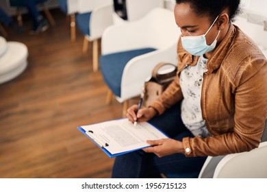 Black woman writing her data in medical document before dental examination. She is wearing protective face mask due to COVID-19 pandemic.  - Powered by Shutterstock