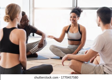 Black Woman Yoga Instructor Talking To Young Yogi Group After Class, Sitting On Floor In Studio And Chatting Together