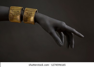 Black woman's hand with gold jewelry. Oriental Bracelets on a black painted hand. Gold Jewelry and luxury accessories on black background closeup. High Fashion art concept 