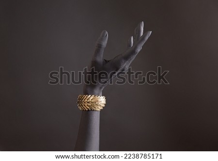 Black woman's hand with gold jewelry. Oriental Bracelet on a black painted hand. Gold Jewelry and luxury accessories on black background closeup. High Fashion art concept 