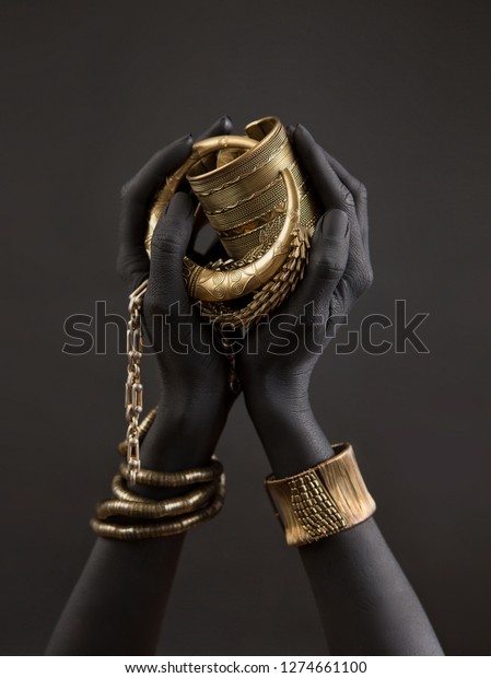 Black\
woman\'s hands with gold jewelry. Oriental Bracelets on a black\
painted hand. Gold Jewelry and luxury accessories on black\
background closeup. High Fashion art concept\
