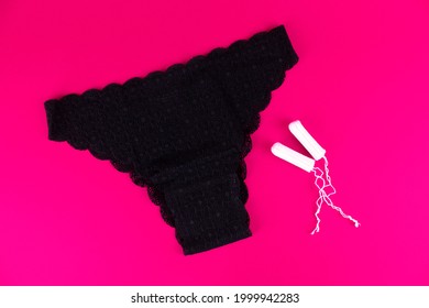 Black women's lace panties and two tampons on a pink background