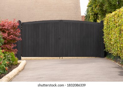 A black, wooden gate bars entry from hedge lined driveway