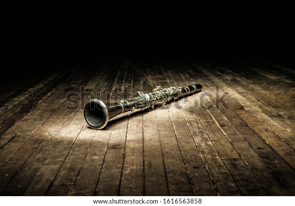 a black woodwind clarinet lies on a dark\
brown wooden stage in the rays of\
light