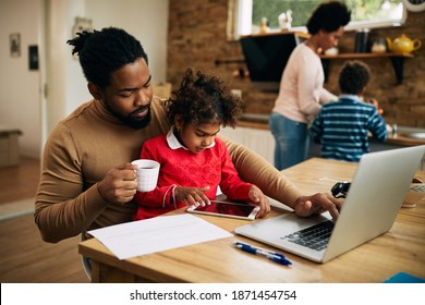 Black working father using laptop while daughter is sitting on his lap and using touchpad at home.  - Powered by Shutterstock