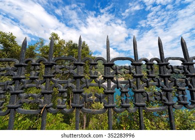 Black Wrought Iron Fence / Old wrought iron fence painted with black color. Blue sky with clouds and green trees on background