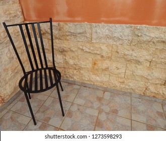 Black Wrought Iron Garden Chair Backed By Lime Stone Wall