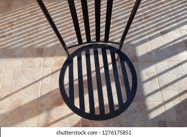 Black Wrought Iron Garden Chair On Tiled Patio Creating Overlapping Shadows.  