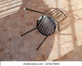 Black Wrought Iron Garden Chair On Tiled Patio Creating Overlapping Shadows.  