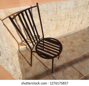 Black Wrought Iron Garden Chair On Tiled Patio Creating Overlapping Shadows.  