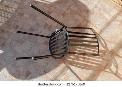 Black Wrought Iron Garden Chair On Tiled Patio Creating Overlapping Shadows.  