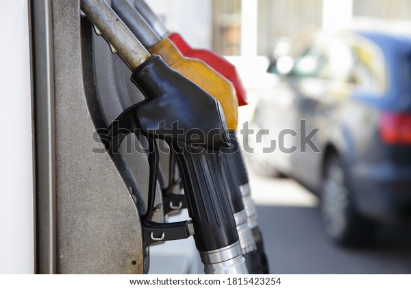 Black, yellow and red fuel guns on gas station\
column on blurred SUV car background on Sunny summer day, gasoline\
vehicle refueling