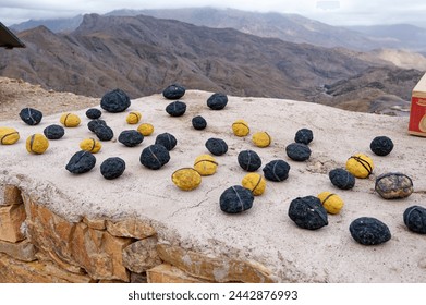 Black and yellow rocks that contain precious minerals, displayed for sale atop a slab, against a backdrop of arid mountains along a scenic moroccan road. - Powered by Shutterstock