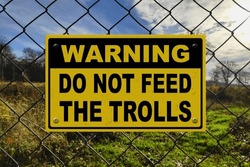 Black And Yellow Warning Sign On A Fence Stating In "Warning - Do Not Feed The Trolls".