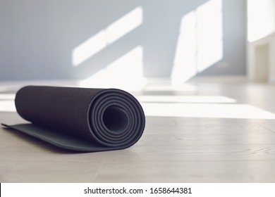 Black yoga mat on the floor of a bright sunny studio.