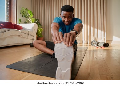 Black Young African American Male Working Out At Home Stretching His Legs Out Before Exercising On His Yoga Mat And Following An Online Class.Keeping Fit.