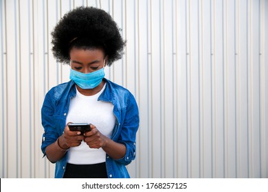 Black young american african woman with black power hair wearing protective mask with smartphone in hands, message text. City grey background. Copy space. - Powered by Shutterstock