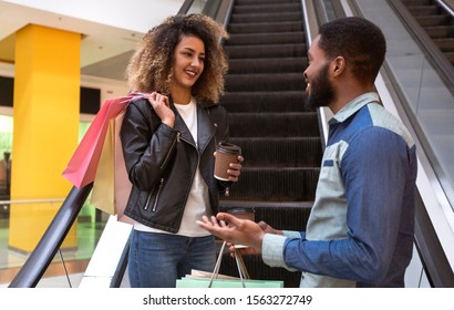 Black Young Couple With Shopping Bags Rising On Escalator And Drinking Coffee