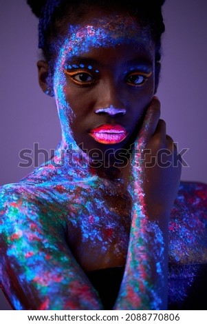 Black young Fashion model woman in neon light, portrait of beautiful model with fluorescent make-up, looking at camera, Art design of female posing in UV, colorful make up. Isolated in studio.