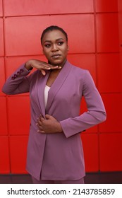 Black young female model posing in purple pants suit on urban red wall background. Looking formal but with a touch of elegance. Street style fashion image with copy space. - Shutterstock ID 2143785859