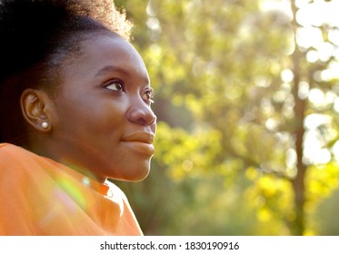 Black young girl, profile face of pretty teenager smiling, with sun lights and sun spots, copy space 