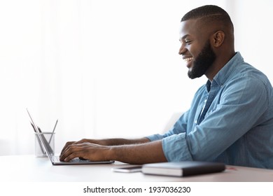 Black Young Man Using Laptop At Home, Enjoying Remote Work, Side View