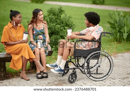 Black young man in wheelchair drinking coffee and telling story to his friends