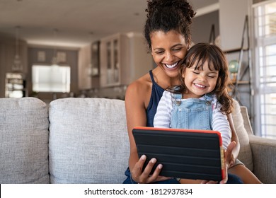 Black young mother and little daughter using digital tablet on couch. Portrait of happy african woman and her cute little girl sitting on sofa together and doing video call on digital tablet. - Powered by Shutterstock