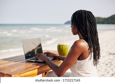 Black Young Woman With Dreadlocks Working On Computer When Sitting At Desk On The Beach