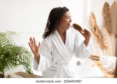 Black Young Woman Enjoying Haircare Singing With Hairbrush Having Fun While Brusing Hair After Shower Standing In Bathroom At Home. Haircare Cosmetics Advert. Female Beauty Routine