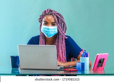 Black young woman in her home office wearing pink braids working on notebook wearing protective mask against corona virus and flu - Shutterstock ID 1719581515