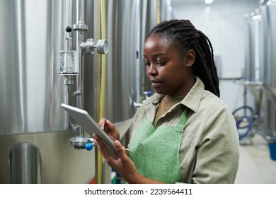 Black young woman referring to tablet computer when checking fermentation process - Powered by Shutterstock