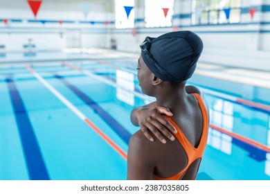 Black young woman touching her sore shoulder at the heated swimming pool - Powered by Shutterstock