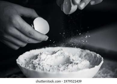 A Black-and-white Image Of A Man Breaking An Egg Shell And Dropping The Yolk Into The Flour In A Bowl. The Process Of Preparing The Dough. Home Cooking.