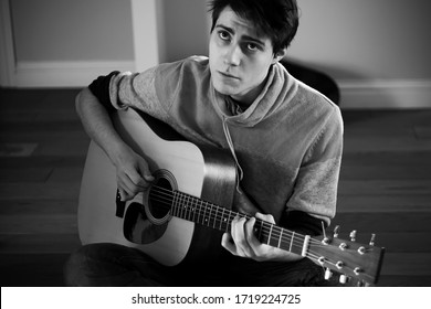 A Black-and-white Image Of A Young Guy In A Sweater Singing A Sad Song And Playing A Tune On An Acoustic Guitar.