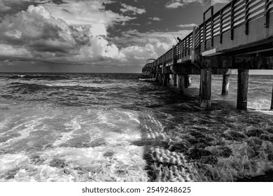 A black-and-white photograph of waves crashing against Lake Worth pier, showcasing dramatic clouds and textured water, highlighting the raw power and beauty of the ocean in a timeless composition. - Powered by Shutterstock