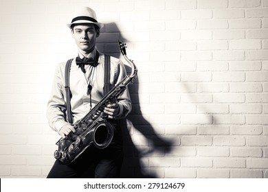 Black-and-white portrait of an elegant musician standing with his saxophone by the brick wall. Art and music. Jazz music. - Powered by Shutterstock