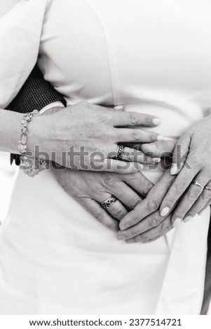 A black-and-white vertical wedding photograph capturing an intimate close-up of the bride and groom's hands, tenderly embracing while showcasing their wedding rings, symbolizing their unbreakable bond