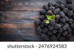 blackberries with a bright green leaf placed among them, arranged on a dark wooden surface