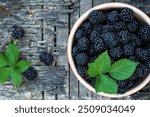 Blackberries with leaves in a ceramic bowl on a wooden background.
