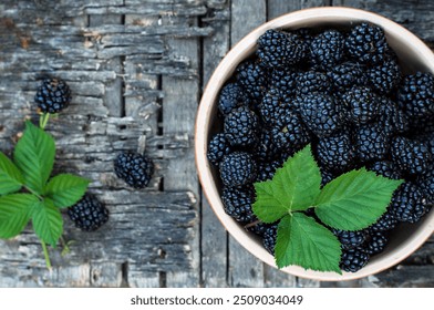 Blackberries with leaves in a ceramic bowl on a wooden background.
