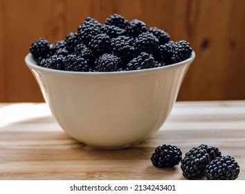 Blackberries in a white deep plate and on a wooden surface. Blackberry. Blackberry fruit close up on wooden table