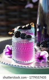 Blackberry Mocktail Garnished With Blackberry Skewer Served On A Metal Tray In Bright Sunlight.